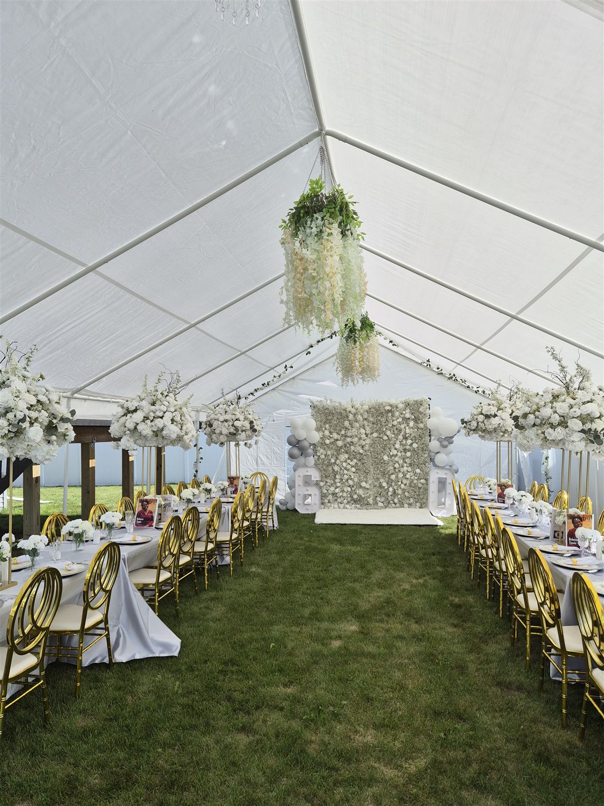 Full tent view with a white flower wall backdrop, gold marquee numbers, and a hanging floral chandelier